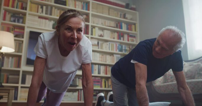 Cinematic shot of happy smiling mature senior couple doing exercises of gymnastics together at home. Concept of healthy lifestyle, fitness, recreation, couple goals, well being, retirement, elderly.