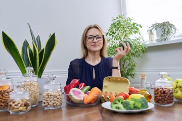 Middle aged woman professional nutritionist sitting at table with foods, avocado