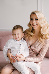 Beautiful young mother and son cuddle and play in smart clothes at home