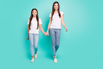 Obraz premium Full length body size photo of two happy young sisters holding hands walking forward isolated vibrant blue color background