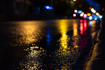 Blurred focus of a freeway during night rain with multicolored out-of-focus lights in the background. Water from the rain and the reflection of lanterns in the city