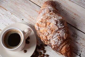 Fresh croissant with a cup of coffee, roasted beans on vintage background