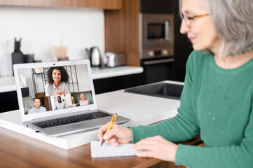 Back view of smiling entrepreneur, aged woman, multiethnic business team, writing notes, on the kitchen, brainstorming, looking for new directions for promotion, on distance, writes down ideas