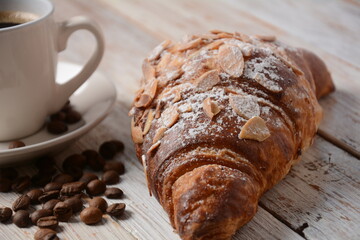 Fresh croissant with a cup of coffee, roasted beans on vintage background