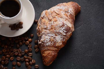 Fresh croissant with a cup of coffee, roasted beans on vintage background