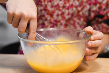 the child prepares food. whipped eggs in a clear bowl, baby hands and a whisk close-up. cooking...