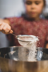 a child prepares food, a girl sifts flour through a sieve over a bowl of dough. focus on the screen, blurry girl. king breakfast at home