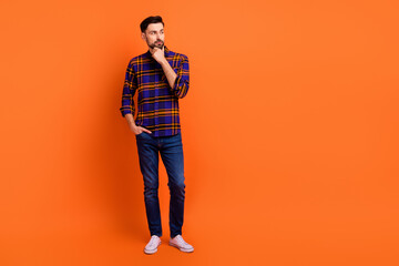 Full length photo of handsome guy arm on chin look interested empty space isolated on orange color...