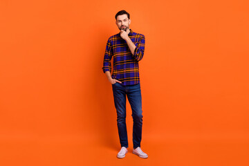 Full body portrait of concentrated person hand on chin look interested camera isolated on orange color background