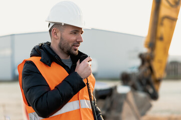 Young engineer talking radio communication (walkie talkie) and wearing a white helmet and...