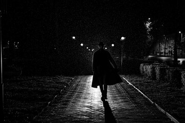 dark silhouette of a male detective in a coat and hat in the rain on a night street