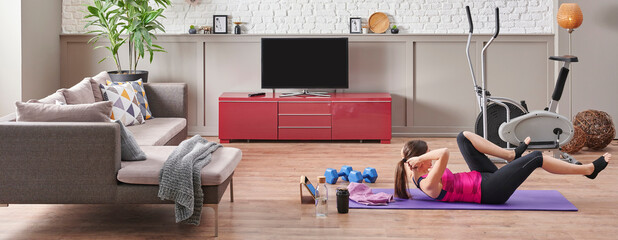 Sportive woman is doing training at home, purple mat, blue dumbbell, decorative living room concept. Healthy lifestyle.