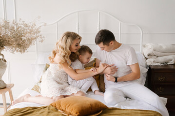 Beautiful young family man woman and son in white clothes play on the bed with a rabbit at home