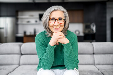 Healthy aged woman with grey hair with glowing blue eyes, elegant glasses, sitting on the pure...