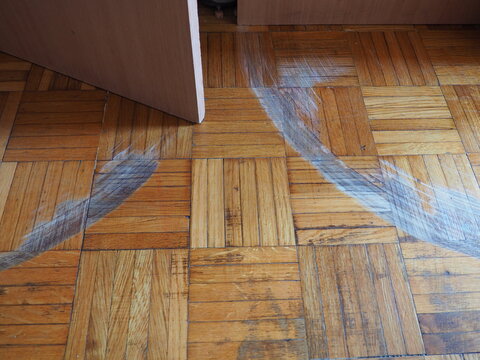 Scratched parquet flooring in the room. Scratches, chips and dents on the floor. Parquet in need of repair. Cabinet doors are scratching the floor. Unadjusted height of furniture doors