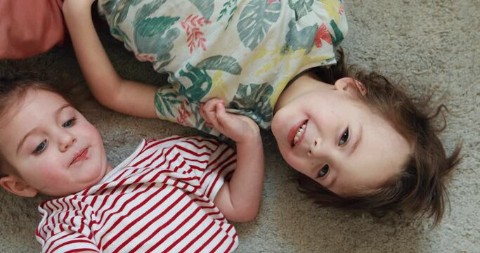 Two children are lying on the floor and laughing. Brother and sister have fun and play around. Siblings at home roll on the carpet