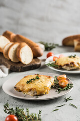 Baked meat and cheese on a plate with French bread baguette with herbs and cherry tomatoes on a light background.