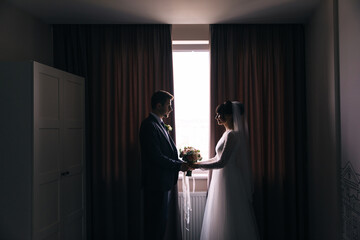Silhouettes of the bride and groom in the interior room, hotel near the window. Wedding portrait of newlyweds.