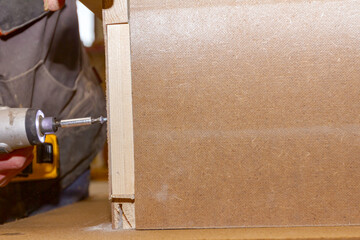 Carpenter uses hand drill, acu power tool and tightens the screws on the wooden door frame.