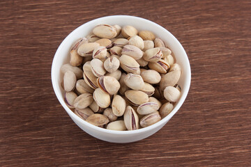 Fried salted pistachios in a white bowl on a wooden table