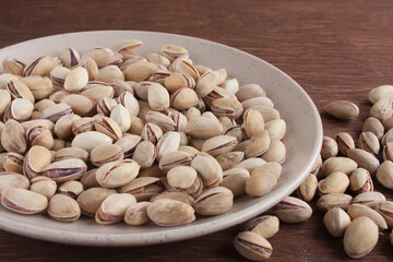 Fried salted pistachios in a light plate on a wooden table