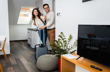 Smiling couple with suitcase arriving in hotel room.