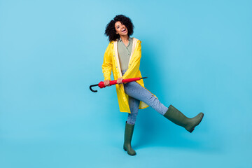 Photo of cute funny dark skin lady dressed waterproof raincoat walking dancing holding umbrella...
