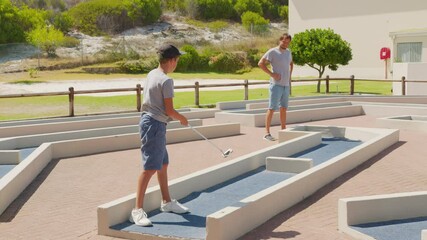 Man with his son playing mini golfers on mini golf course at summer day.