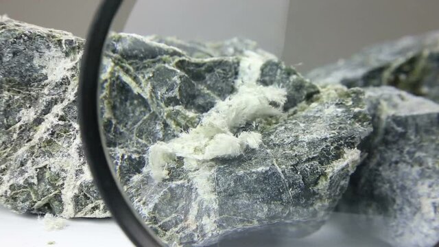 Hand with magnifying glass examines asbestos fibers in stone
