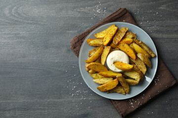 Plate with potato wedges and sauce on dark textured background