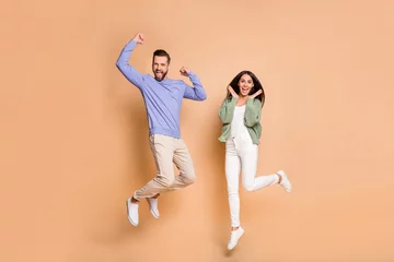 Fotobehang Full length body size view of nice cheerful lucky partners couple jumping having fun isolated on beige pastel color background © deagreez
