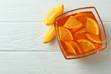 Bowl of orange jelly with orange slices on white wooden background