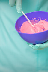 Close up of beautician's hands prepares pink alginate mask mixing in the blue bowl