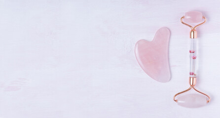 Pink Gua Sha facial massage tools. Rose Quartz jade roller on pink wooden background. Copy space