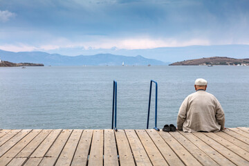Old man sit on the wooden dock. Looking the horizon.
Edit

