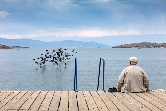 Old man sit on the wooden dock. Looking the horizon.
Edit
