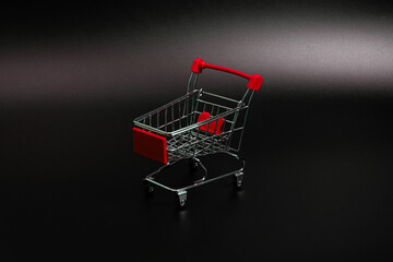 Small red shopping cart on a black background. Copspace