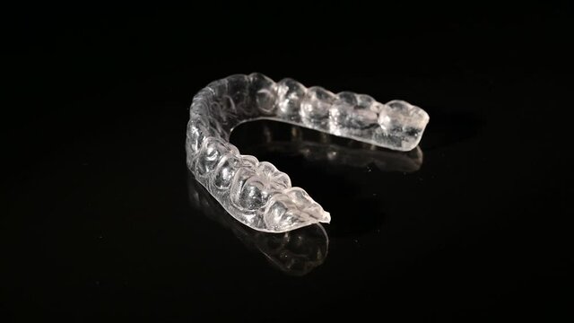 Removable plastic retainers for bite correction revolve against a black background