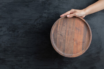 Fototapeta premium Holding a round wooden board on black background