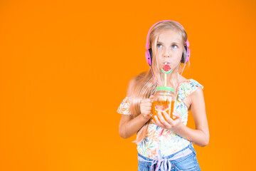 Study portrait of a blonde girl listening to music with pink headphones while drinking a fruit...
