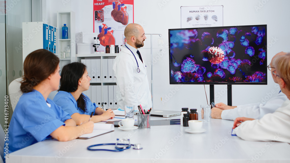 Poster doctor presenting virus development on digital screen in front of colleagues pointing on monitor in 