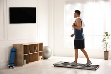 Fototapeta na wymiar Sporty man training on walking treadmill while watching TV at home