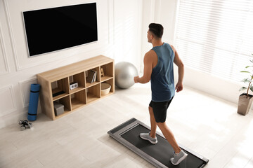 Fototapeta na wymiar Sporty man training on walking treadmill while watching TV at home