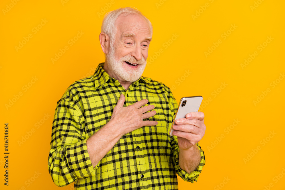 Poster Photo of old man grandfather hand on chest happy smile grateful look browse cellphone isolated over yellow color background