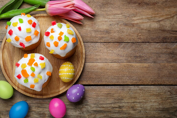 Fototapeta na wymiar Traditional Easter cakes, tulips and colorful eggs on wooden table, flat lay. Space for text