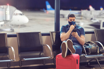 Man wearing face mask sitting in airport departure terminal using mobile phone tracking app while...