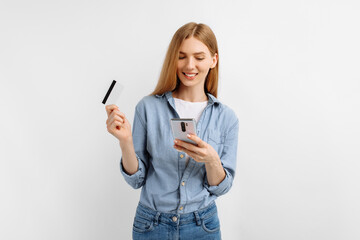 young woman holding credit card while using mobile phone on white background