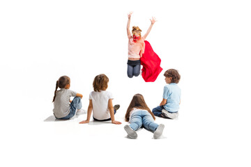 Flying. Child pretending to be a superhero with her friends sitting around her. Kids excited, inspired by their strong, brave friend in red coat isolated on white background. Dreams, emotions concept.