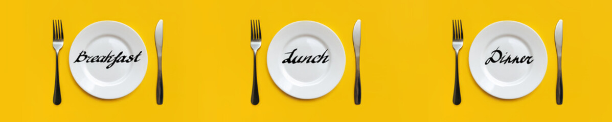 On the yellow tablecloth are three sets of white plates, stainless steel forks, knives. Words - breakfast, lunch, dinner. Table setting concept, top view. Intermittent fasting, diet.Copy space, mockup