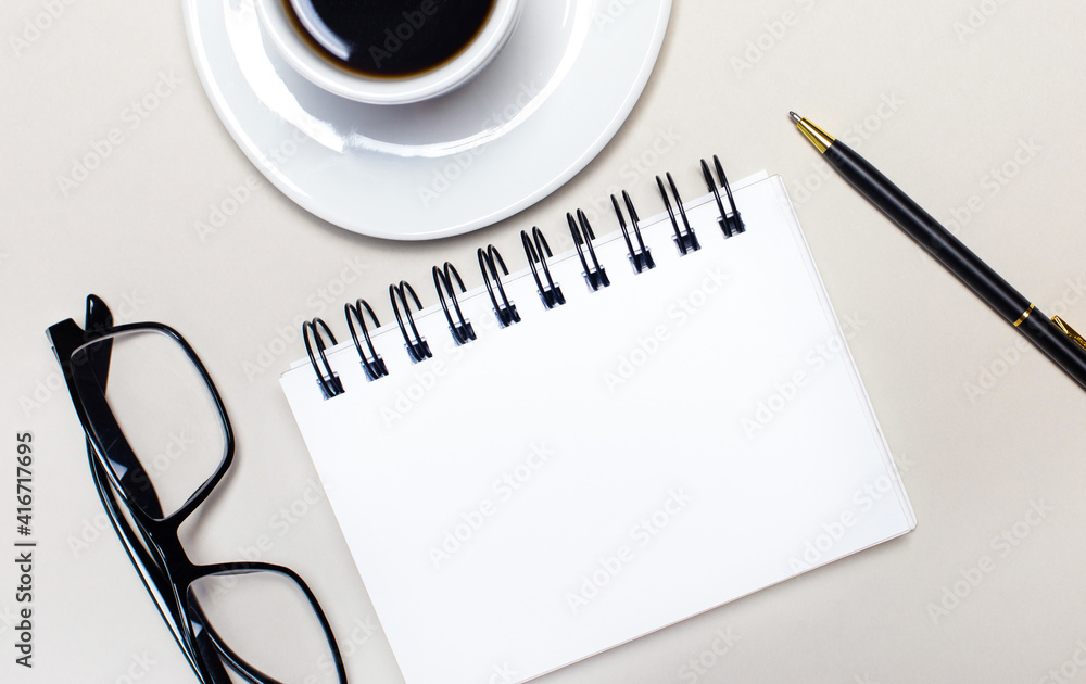 Poster glasses, a white cup with coffee, a blank white notepad for inserting text and a ballpoint pen lie o